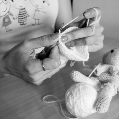 A person handcrafting a soft knitted toy using white wool indoors.