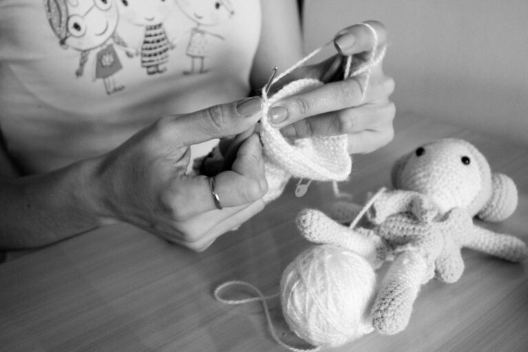 A person handcrafting a soft knitted toy using white wool indoors.